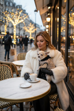 Cagnolina con cappottino in braccio a donna ricca al caffè di Parigi in inverno
